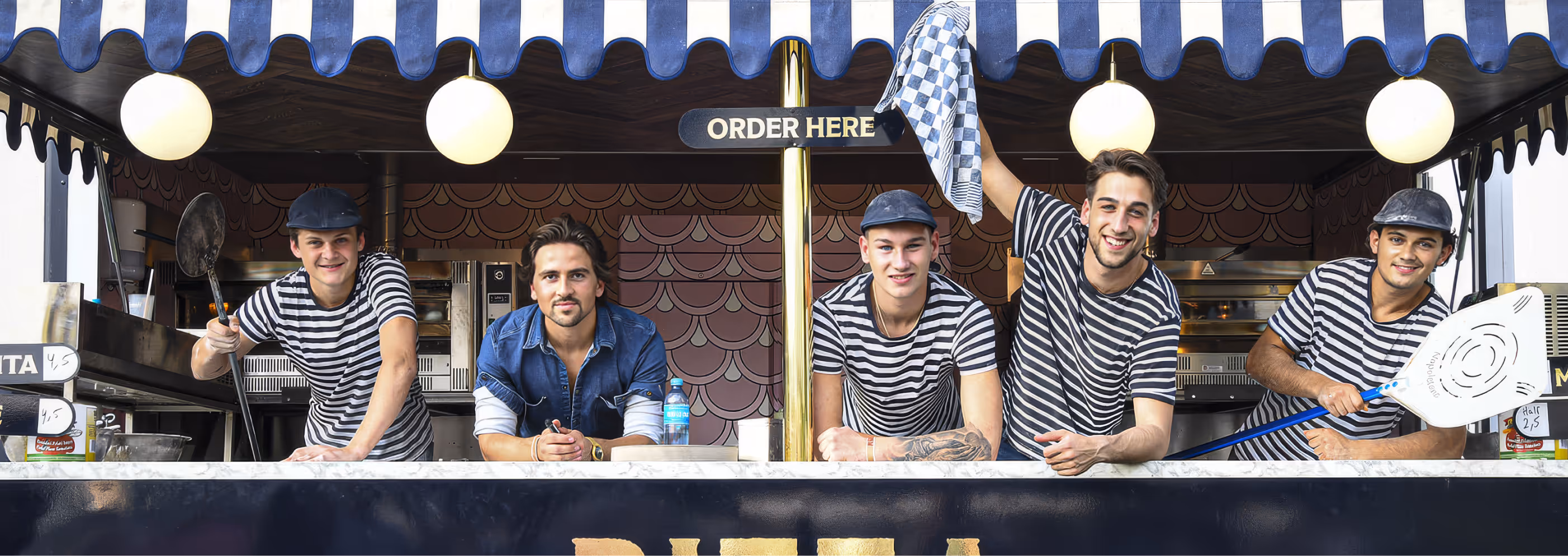 Five young men smiling at a pizza stand counter under a striped blue and white awning with an 'Order Here' sign above them.