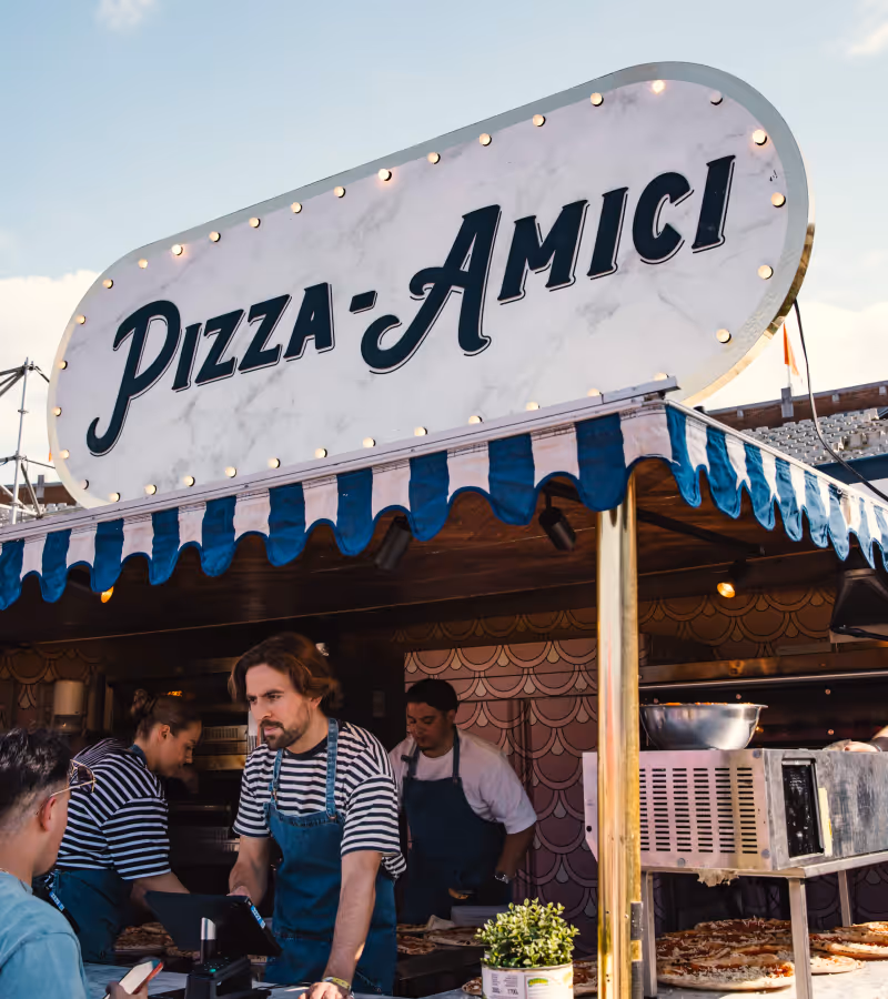 Food stall with sign 'Fornello' and workers serving customers.
