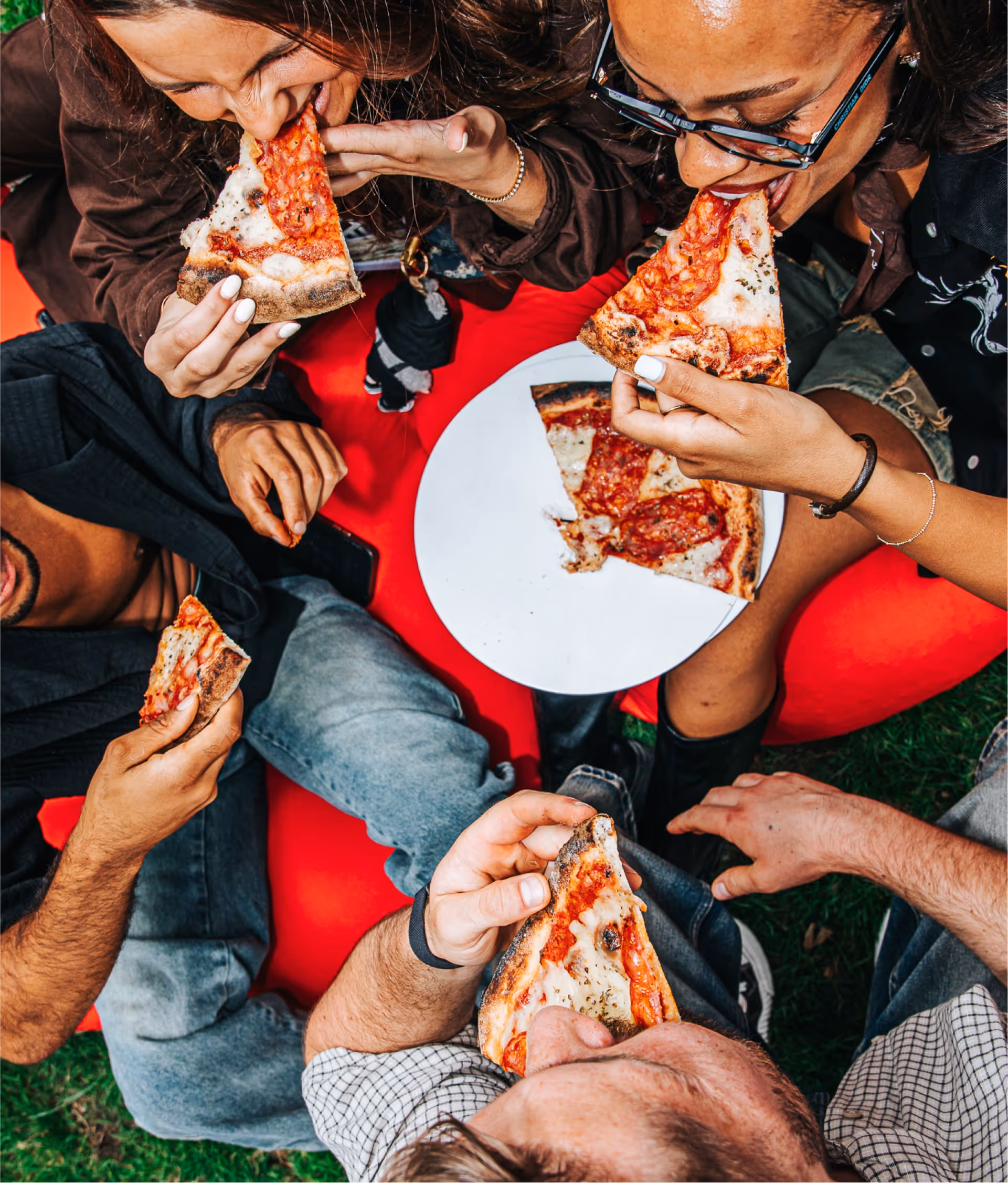 Vier mensen genieten samen van het eten van gesneden pizza buiten op een rood zitkussen.